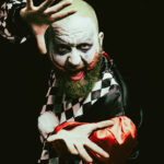 Expressives Porträt eines kostümierten Mannes mit Joker-artigem Make-up und dramatischer Geste im Studio