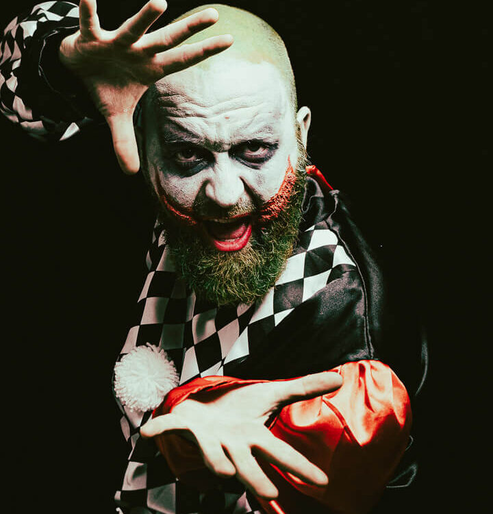 Expressives Porträt eines kostümierten Mannes mit Joker-artigem Make-up und dramatischer Geste im Studio