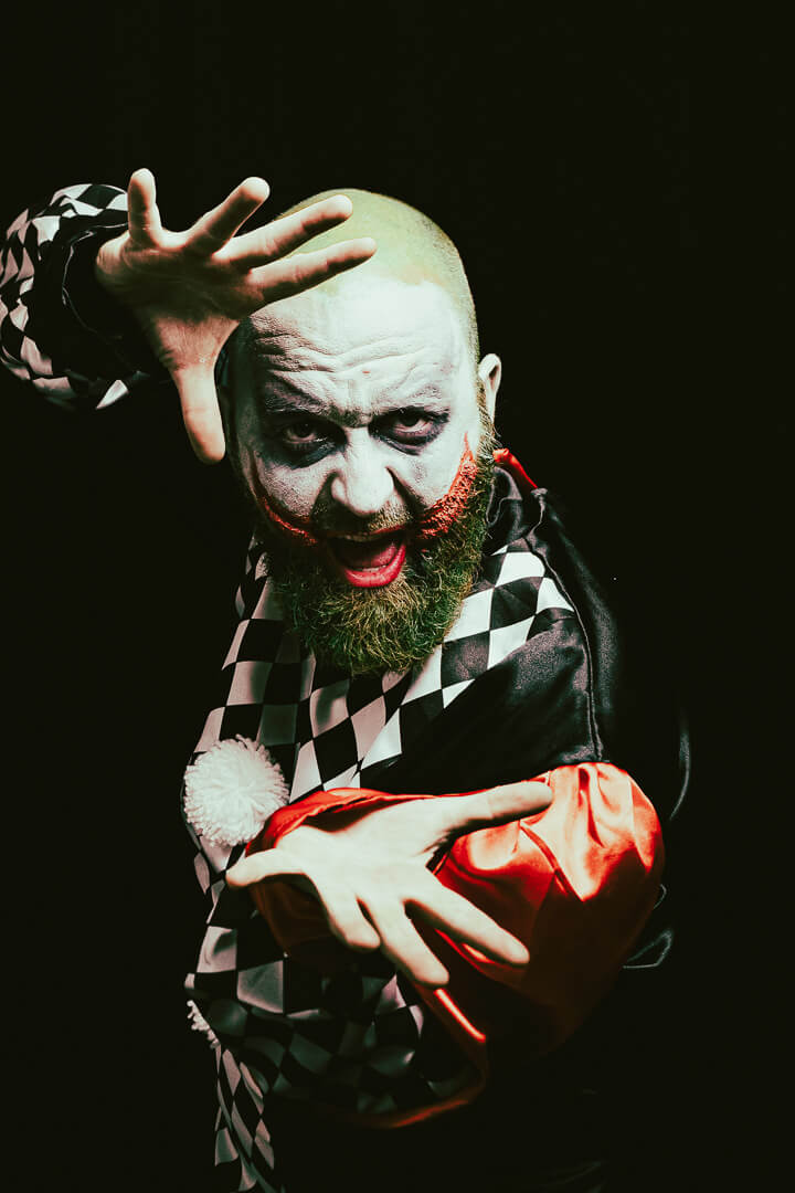 Expressives Porträt eines kostümierten Mannes mit Joker-artigem Make-up und dramatischer Geste im Studio