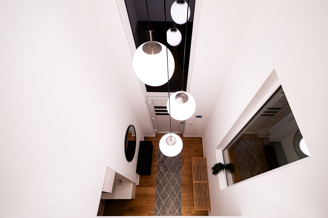 Blick in einen offenen, hell erleuchteten Eingangsbereich mit moderner Hängelampe und Holzdetails in einem Neubau. Fotografiert von Sebastian Leyser.