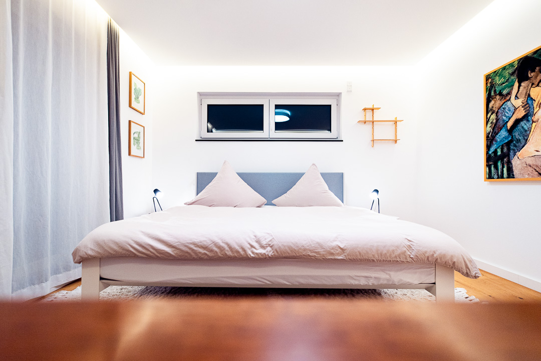 Minimalistisch eingerichtetes Schlafzimmer mit großem Doppelbett, warmem Licht und klarer Linienführung. Immobilienfotografie von Sebastian Leyser.