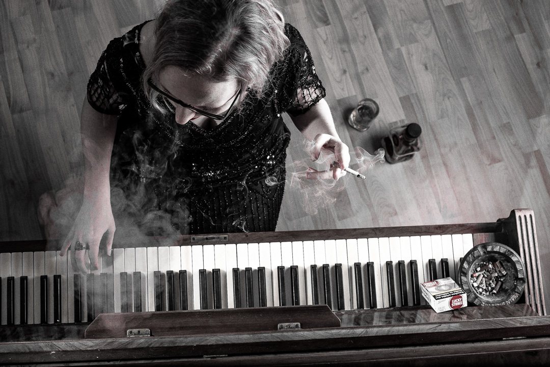 Frau mit Zigarette spielt rauchend Klavier – ausdrucksstarke Schwarzweißaufnahme mit melancholischer Atmosphäre.
